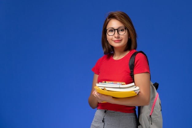 front view female student red shirt with backpack holding books files smiling blue wall 140725 38370