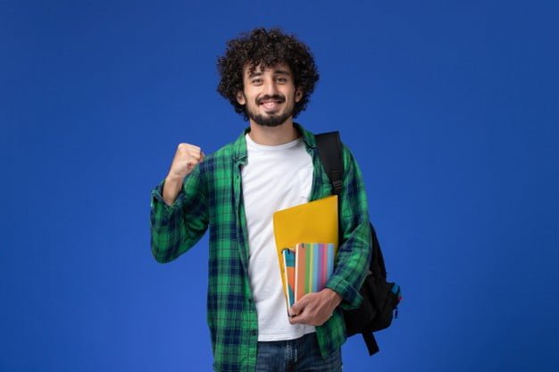 front view male student wearing black backpack holding copybooks files blue wall 140725 42636